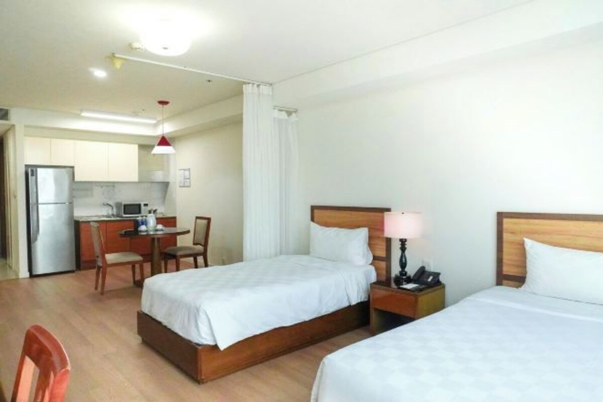 Een hotelkamer met twee bedden, een kleine kitchenette, een eettafel en een stoel.
