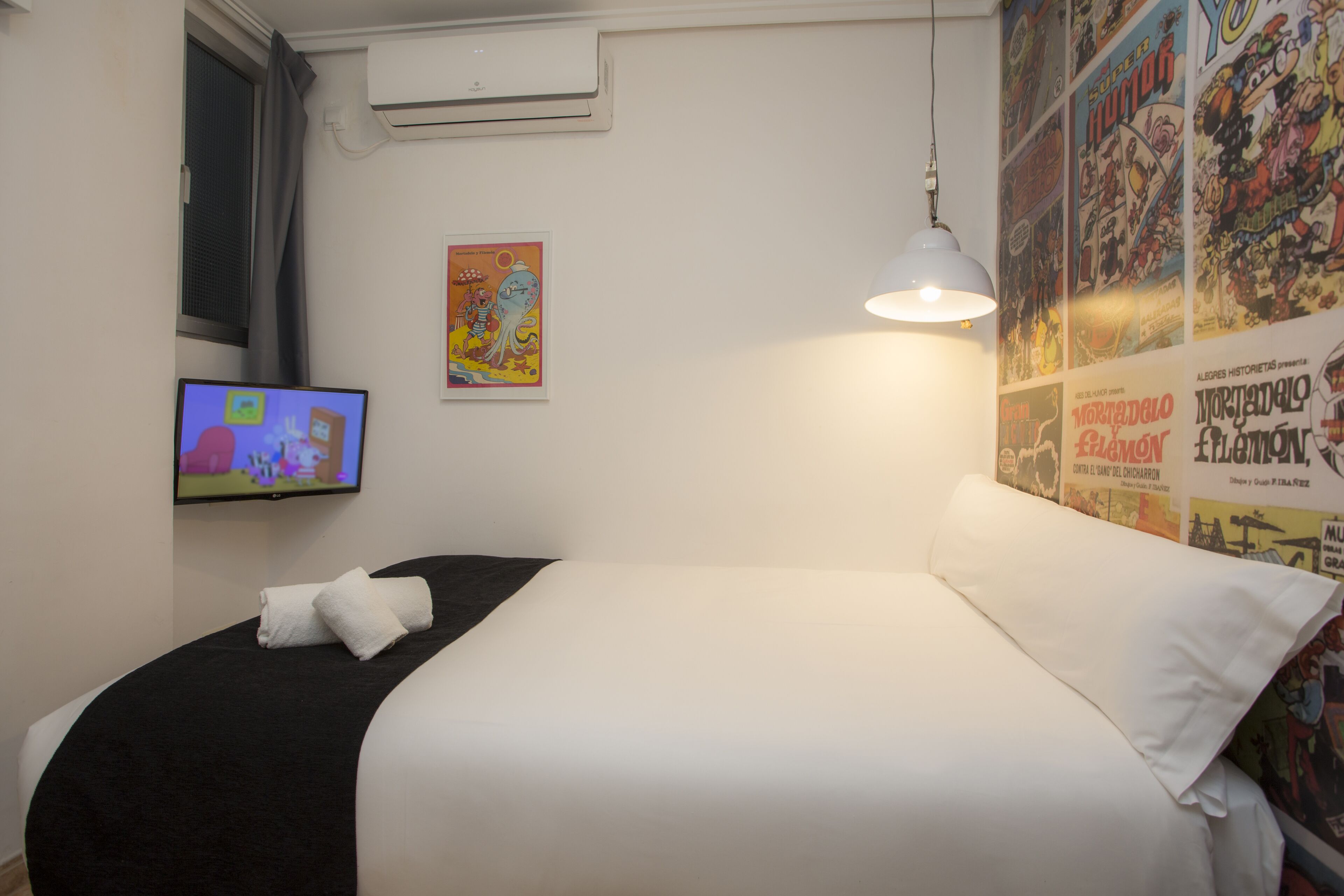 Habitación de hotel con cama, televisión en la pared y un cartel de un personaje de dibujos animados.