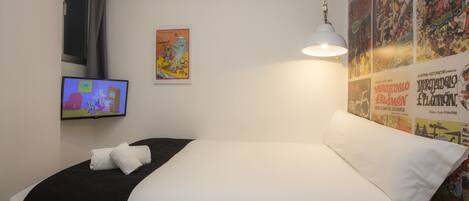 Habitación de hotel con cama, televisión en la pared y un cartel de un personaje de dibujos animados.