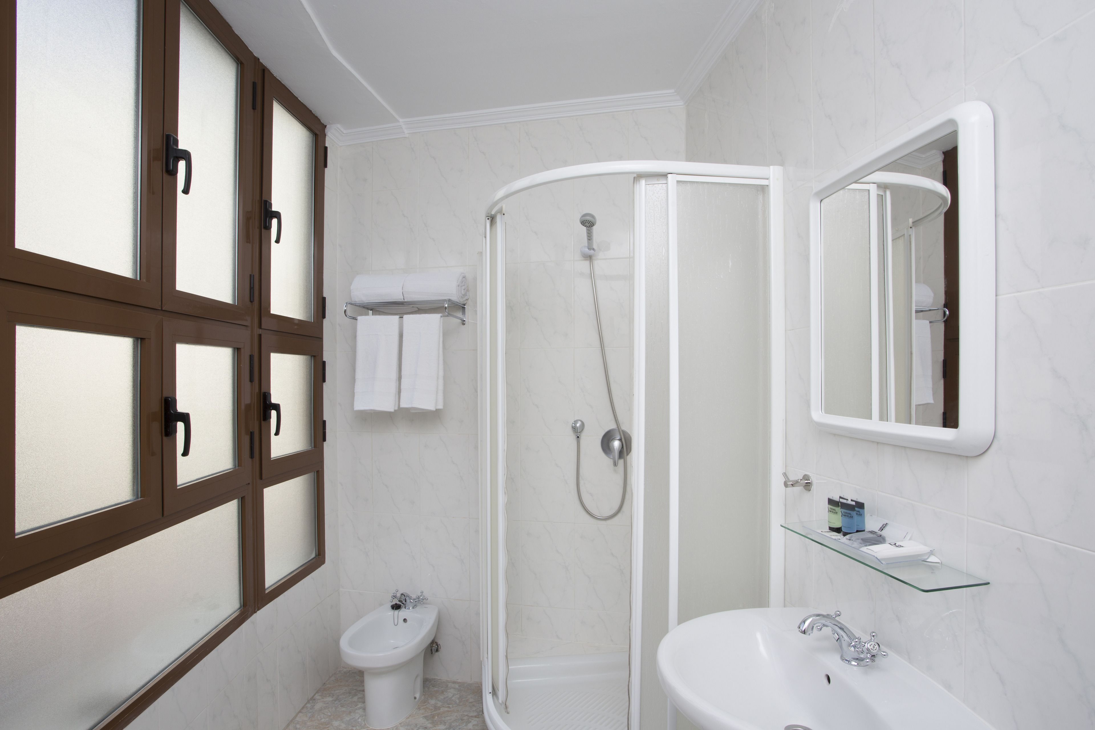 A modern bathroom with a glass-enclosed shower, a pedestal sink, and a mirror above the sink.
