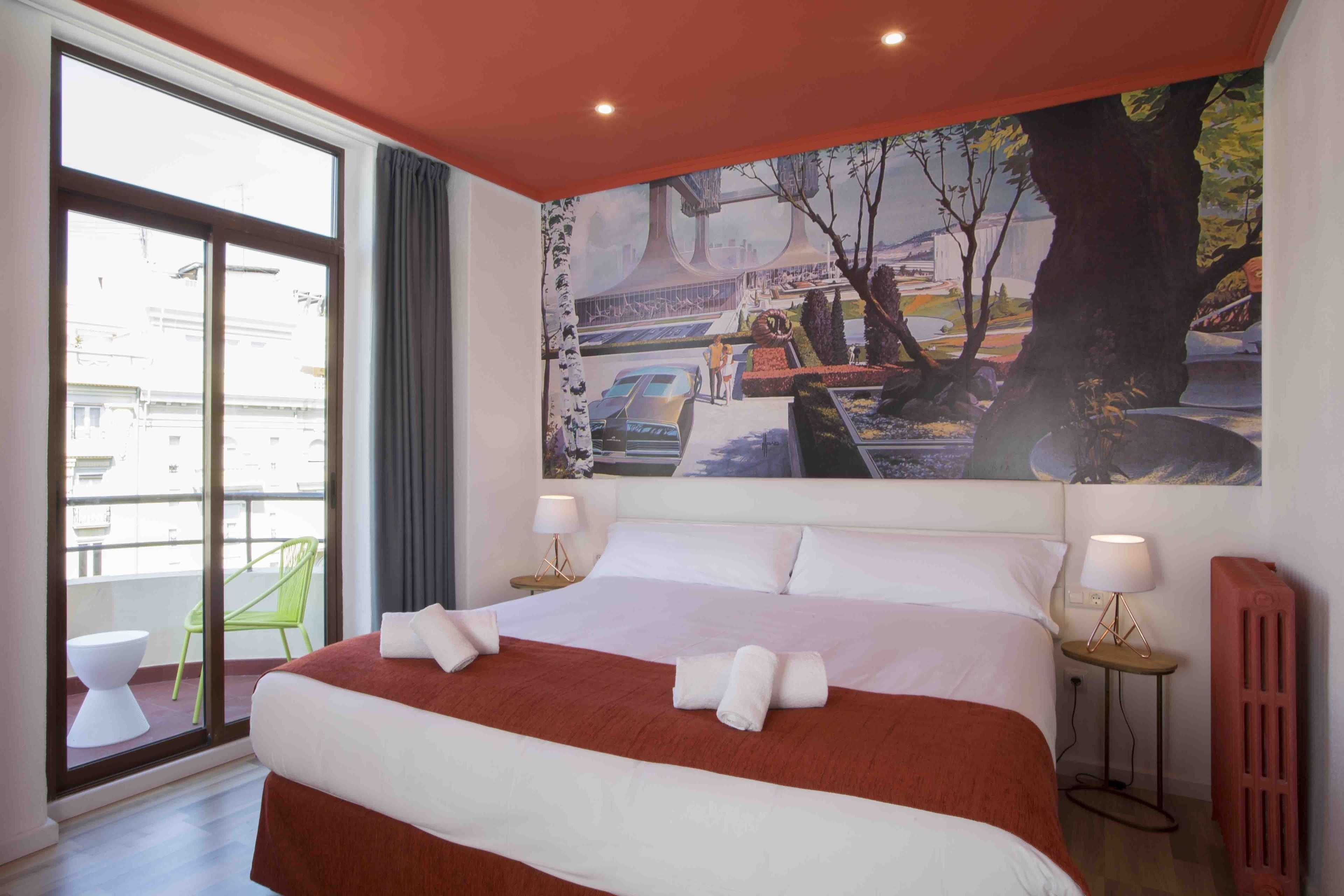 A hotel room with a large bed, two bedside tables with lamps, a view of the city through a large window, and a painting on the wall.