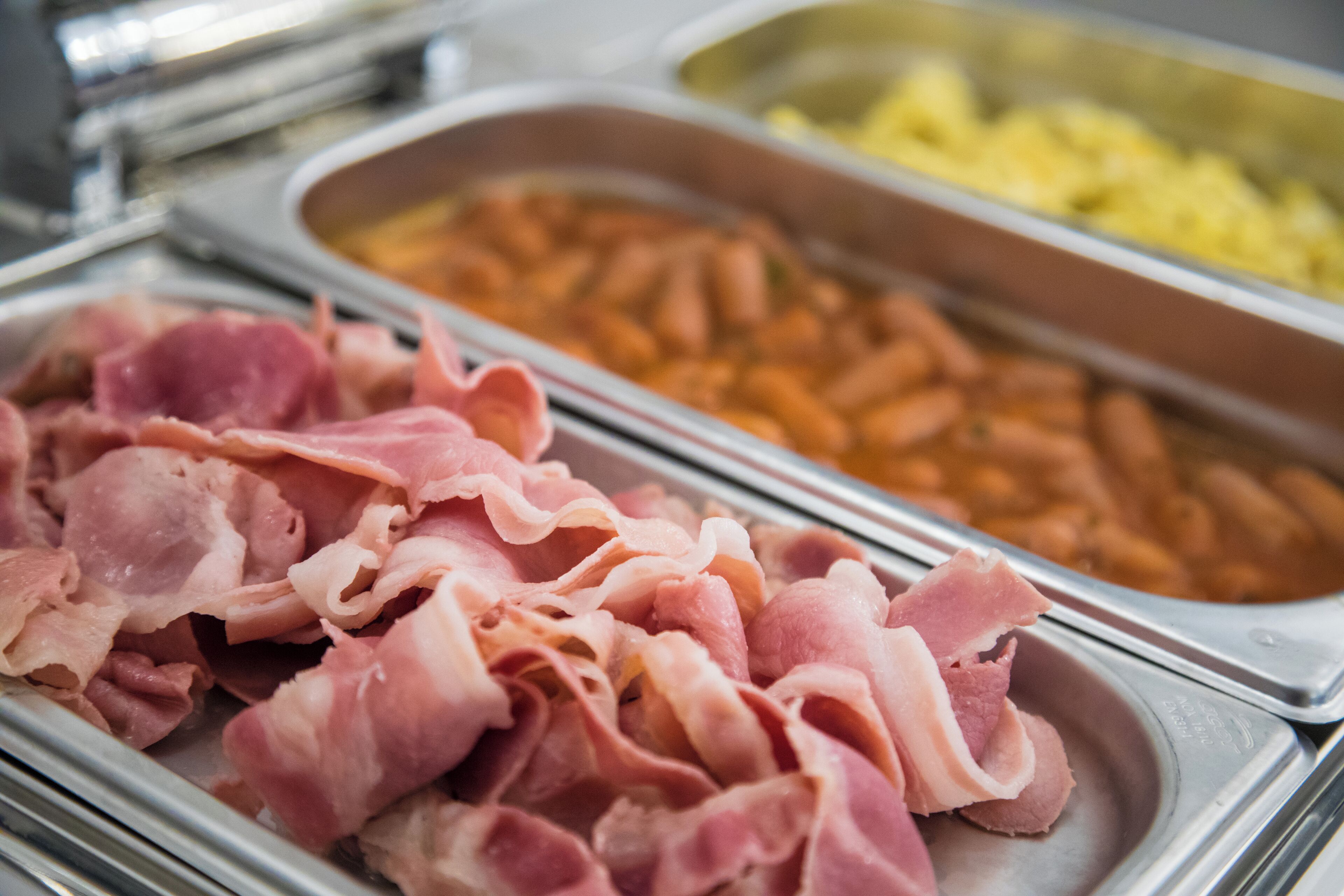 Een buffet met diverse gerechten, waaronder spek, bonen en aardappelen.