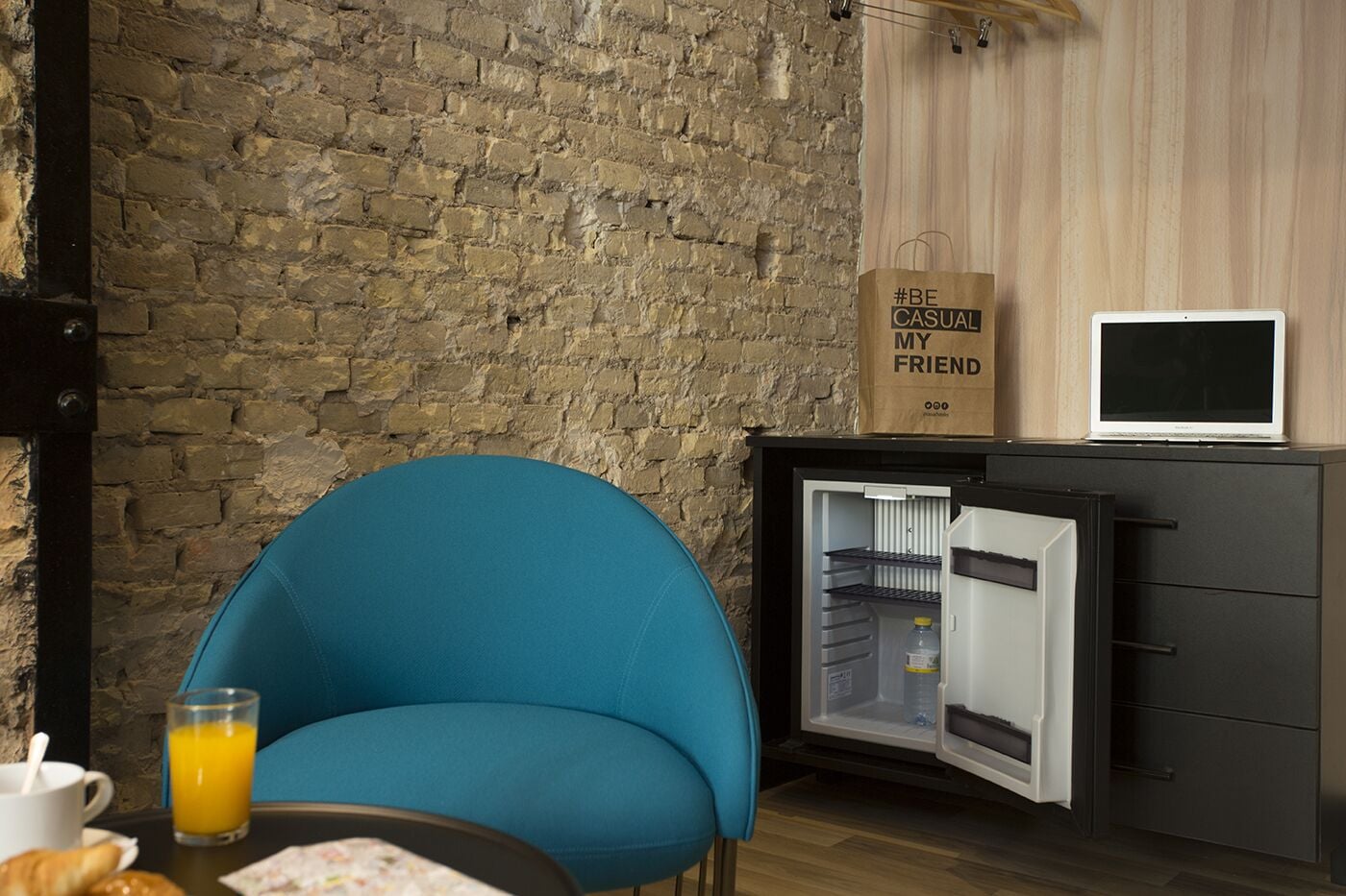 A compact kitchenette with a fridge, a small table with a glass of orange juice, and a blue chair.