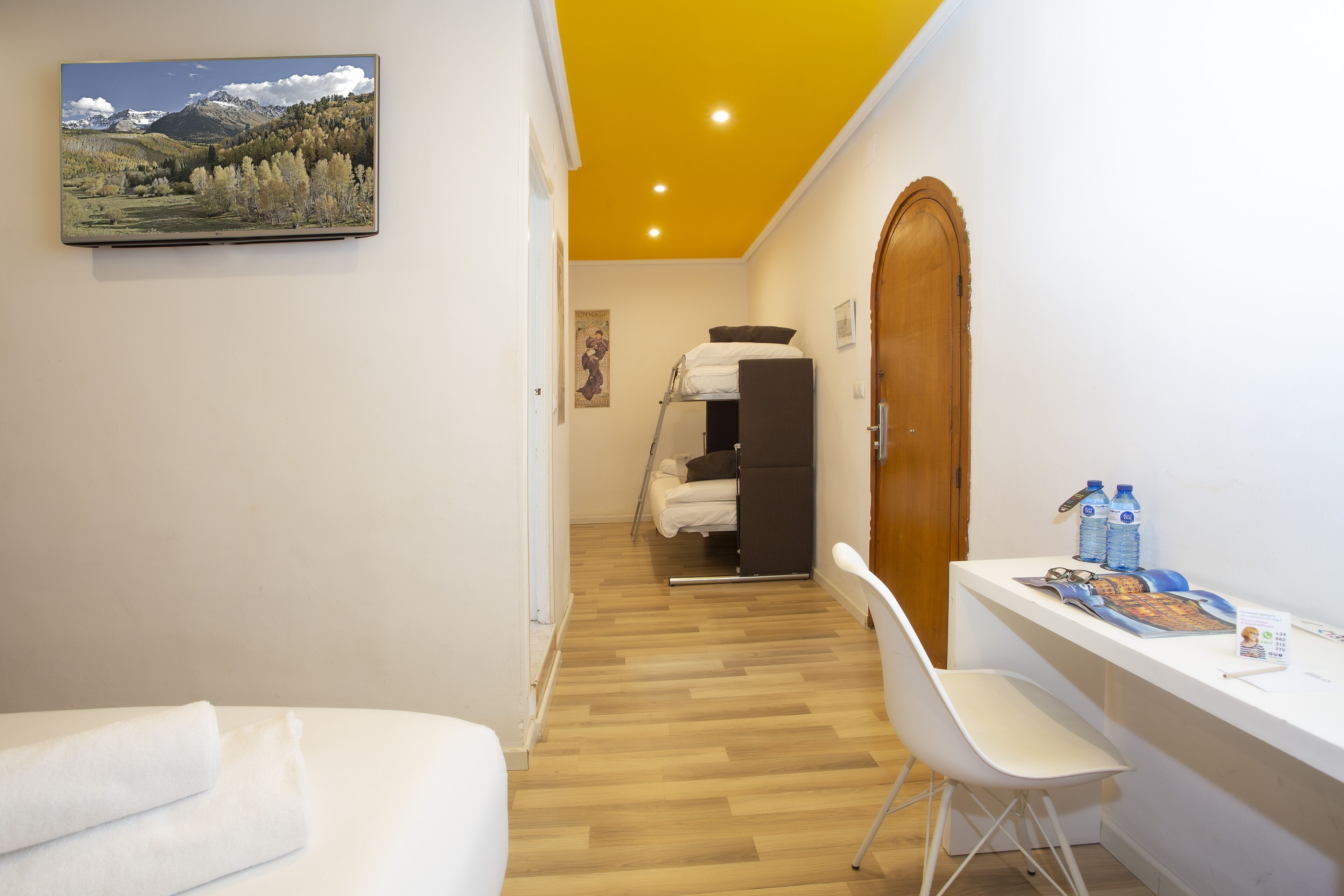 Une chambre d’hôtel avec un lit, un bureau et une chaise, une porte en bois et un tableau au mur.