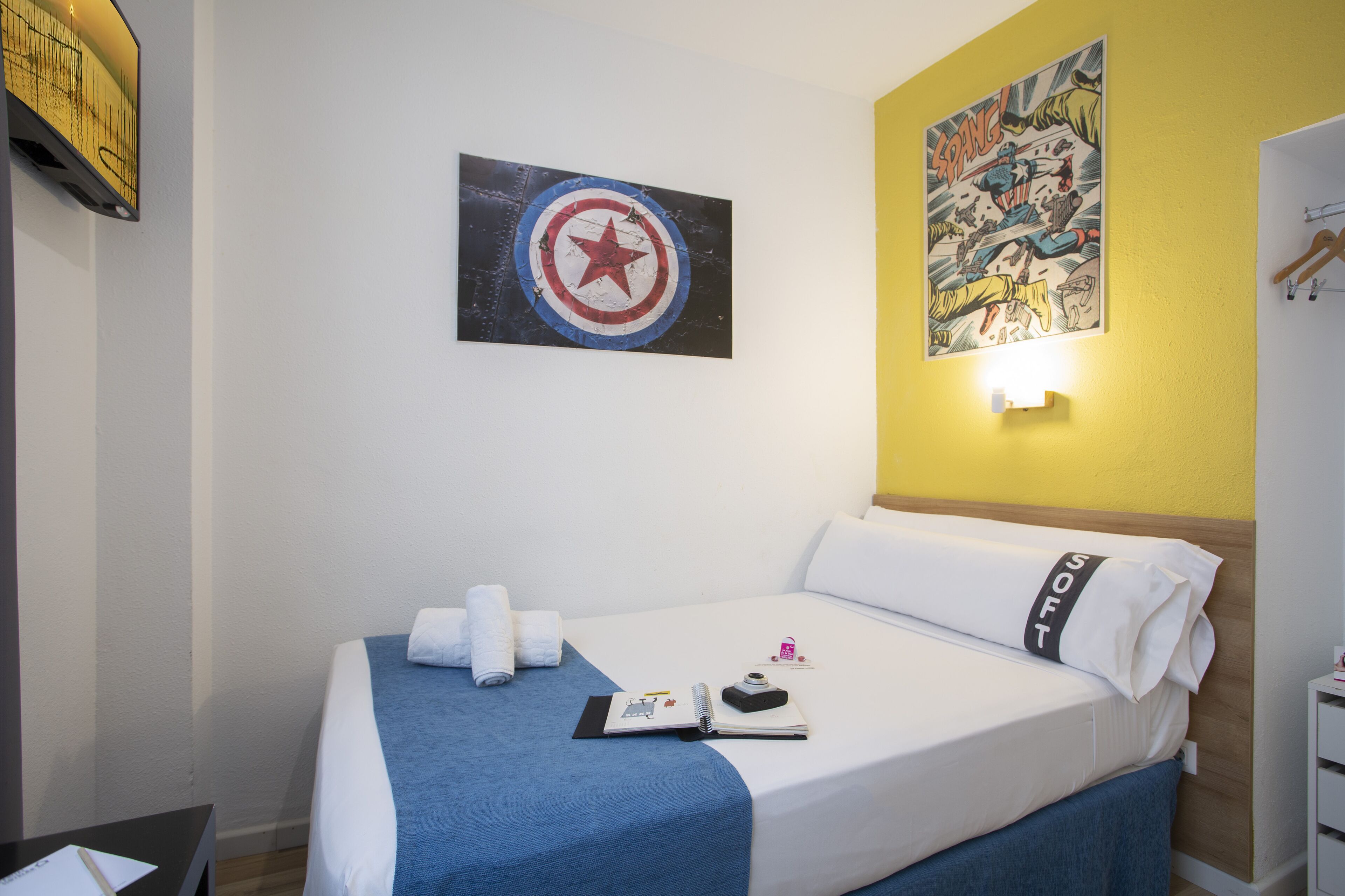 A hotel room with a bed, a wall-mounted artwork, a bedside table, and a nightstand.