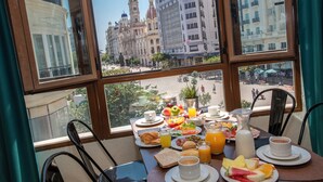 Una mesa de desayuno con diferentes alimentos y una vista de edificios históricos a través de una ventana.