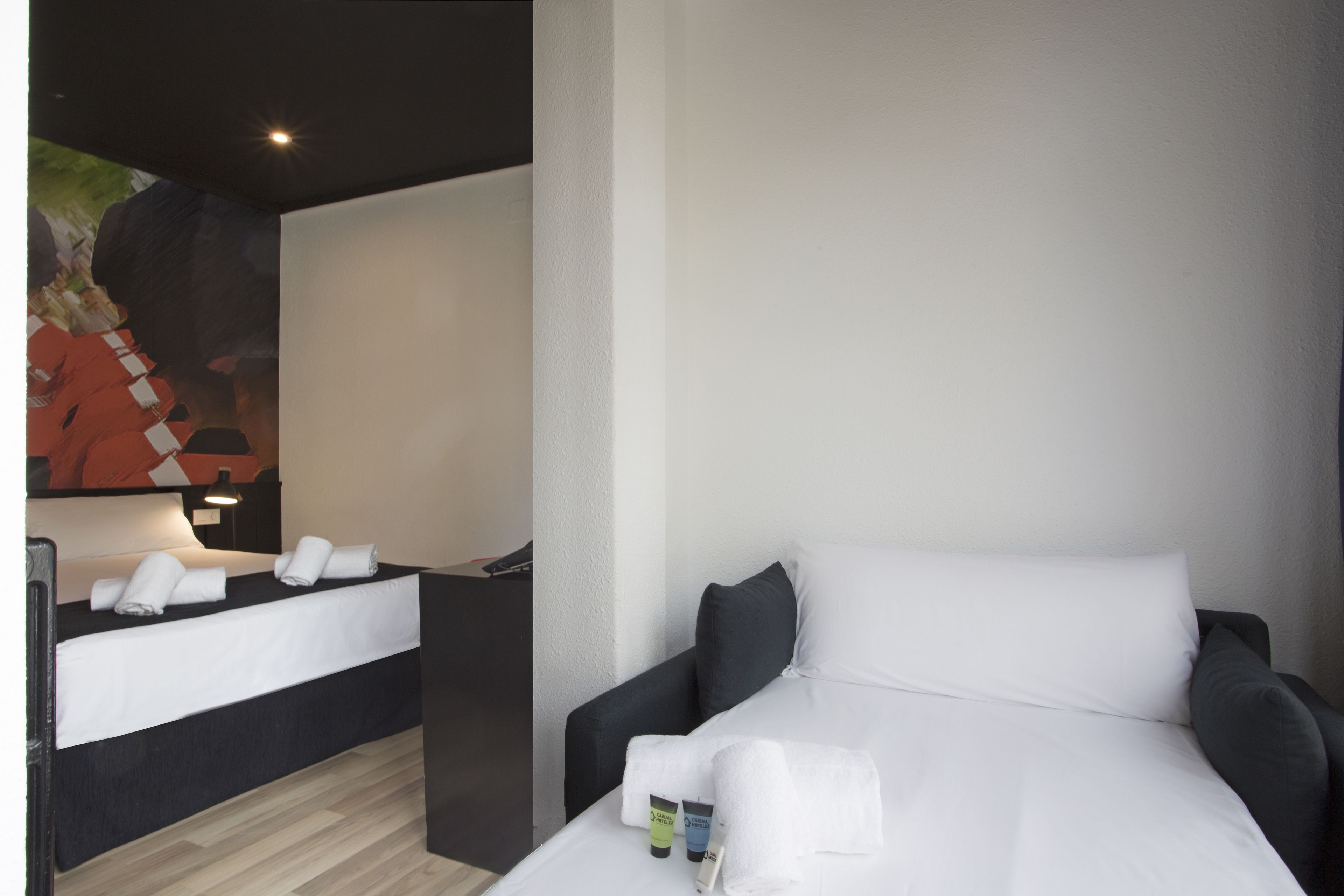 Una habitación de hotel con una cama, una mesita de noche, una lámpara de pared y un cuadro en la pared.