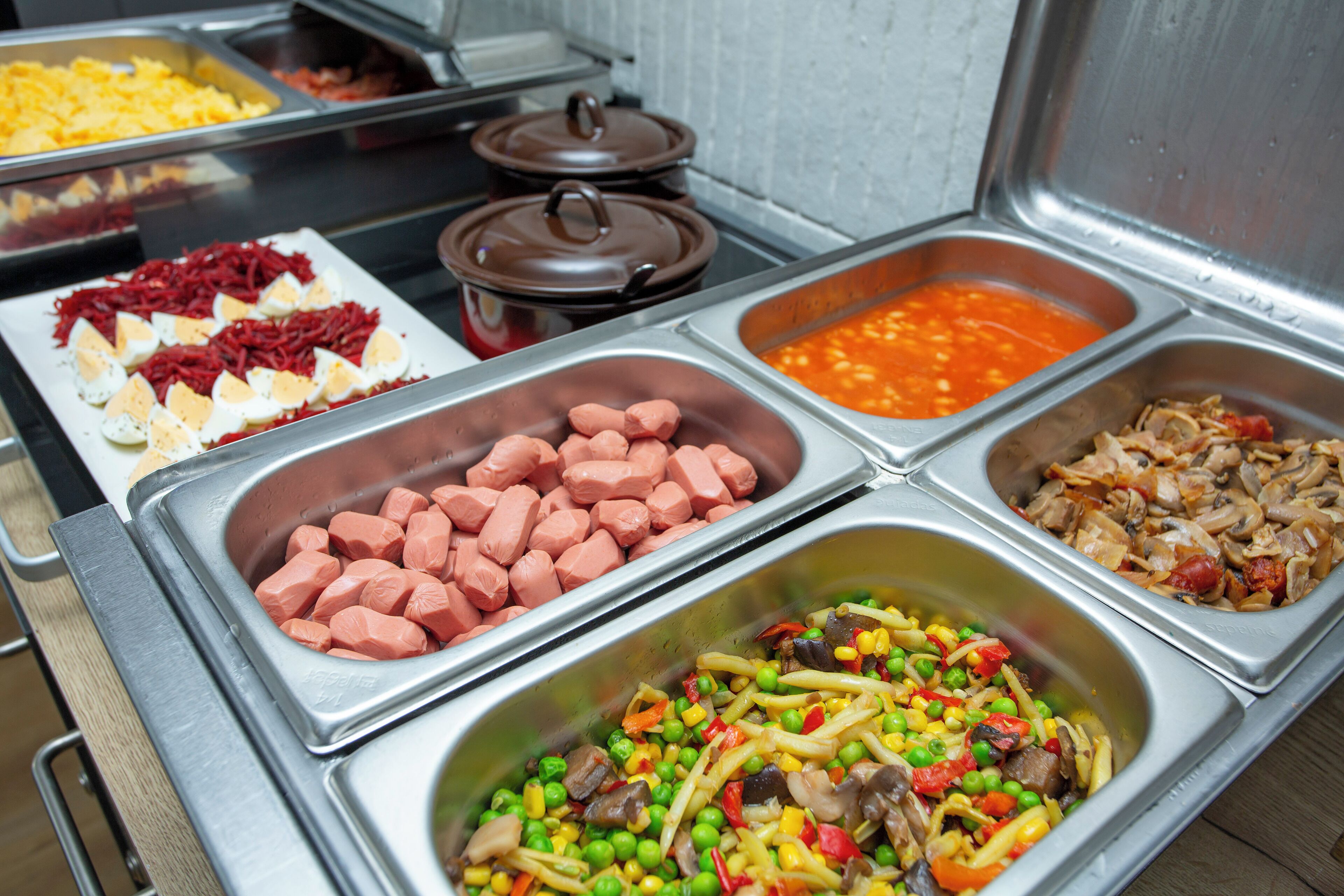 Un buffet proposant une variété de plats, notamment des œufs, des saucisses et un plat de légumes sautés.