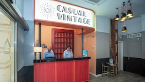 A reception desk with a red and black color scheme, a sign reading "CASUAL VINTAGE," and a wooden wall with a shelf.