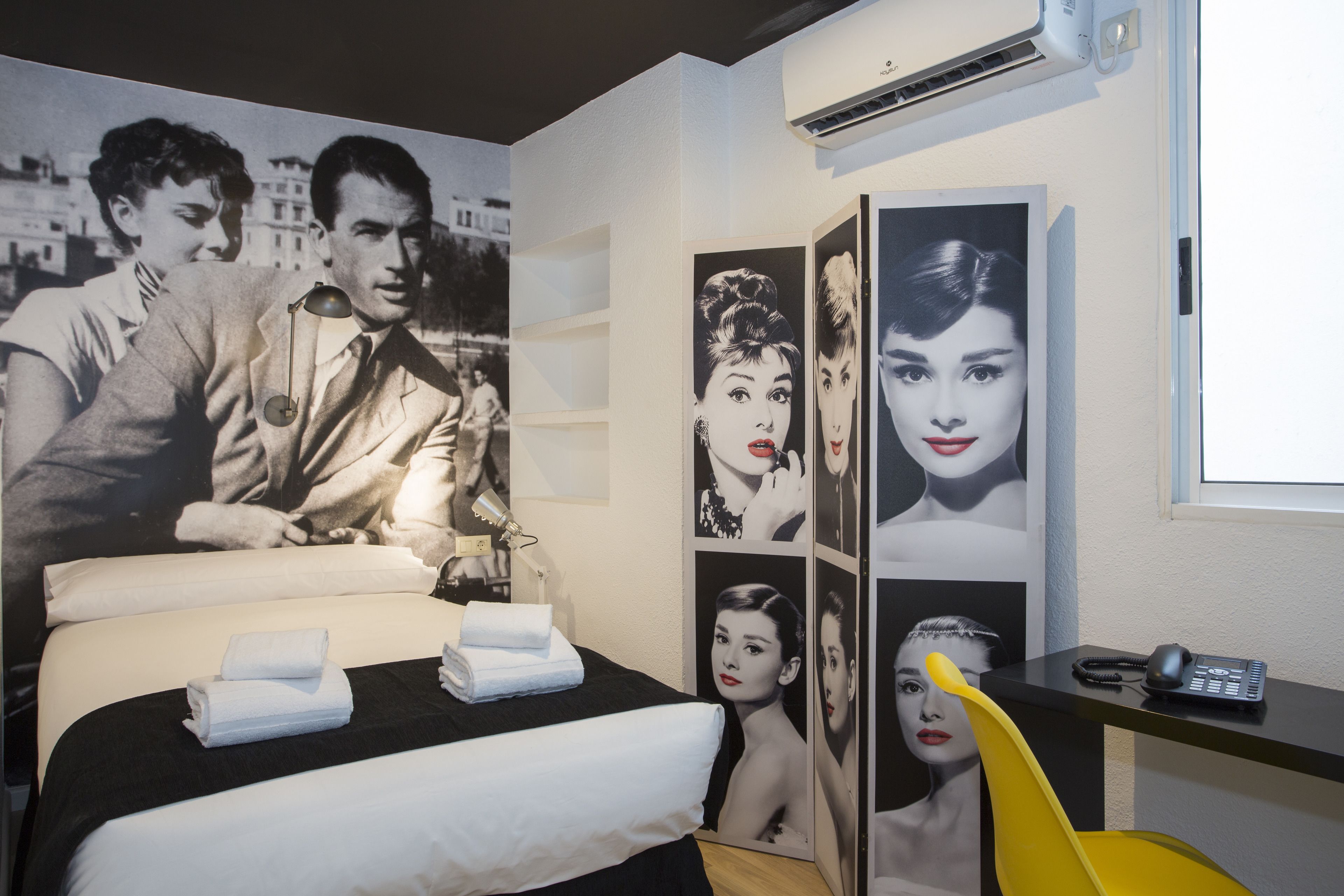 A hotel room with a large bed, a desk with a telephone, and a wall decorated with black and white photographs.