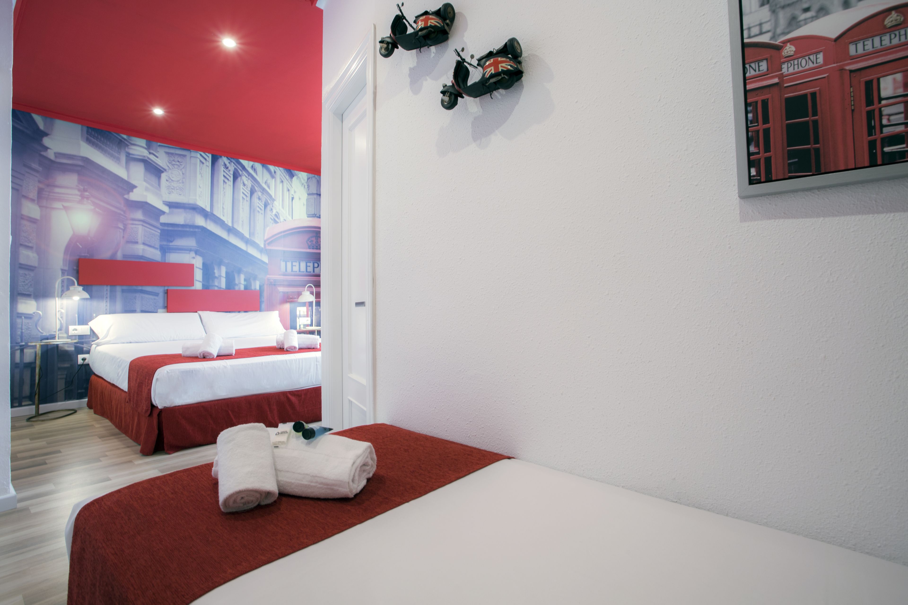 A hotel room with a bed, a red wall, and a painting of a red telephone booth.