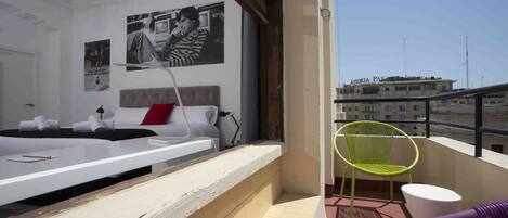 A modern hotel room with a bed, a desk, and a balcony with chairs.