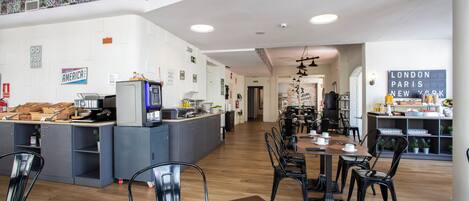 Una cafetería moderna con una barra central, varias zonas de estar y un cartel que enumera destinos turísticos populares.