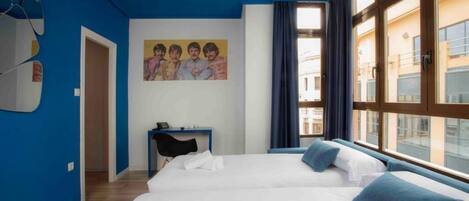 A hotel room with two beds, a desk, and a painting on the wall.
