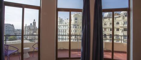 Una habitación con grandes ventanales que dan a un paisaje urbano, con un balcón que tiene una mesa y sillas.
