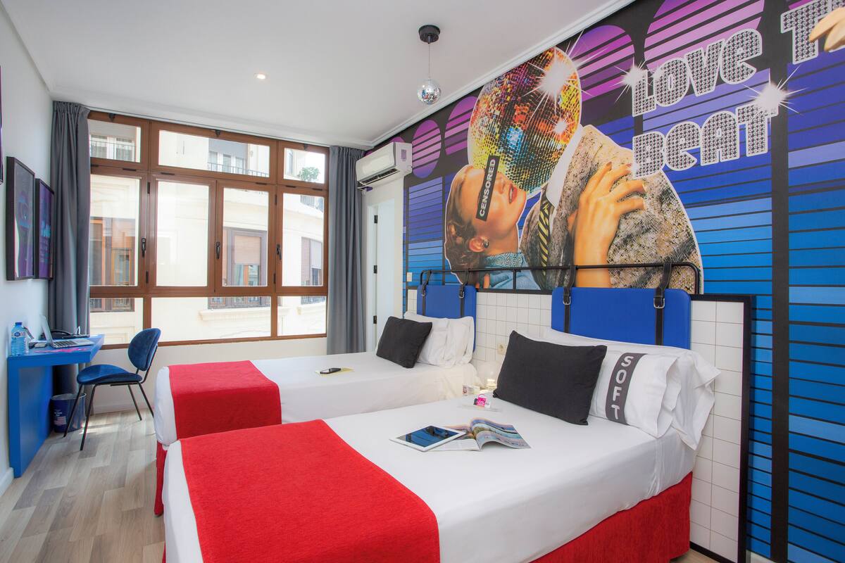 Une chambre d’hôtel avec deux lits, un bureau et une grande fenêtre.