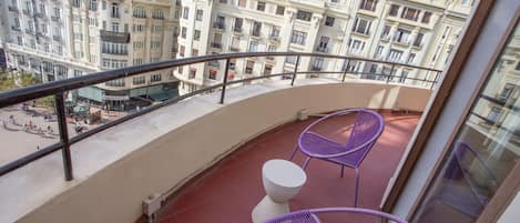 A balcony with a red floor, two purple chairs, and a white stool.