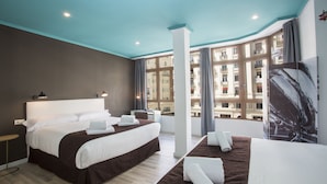 Una habitación de hotel moderna con una cama grande, un área de descanso y vistas de la ciudad a través de amplias ventanas.