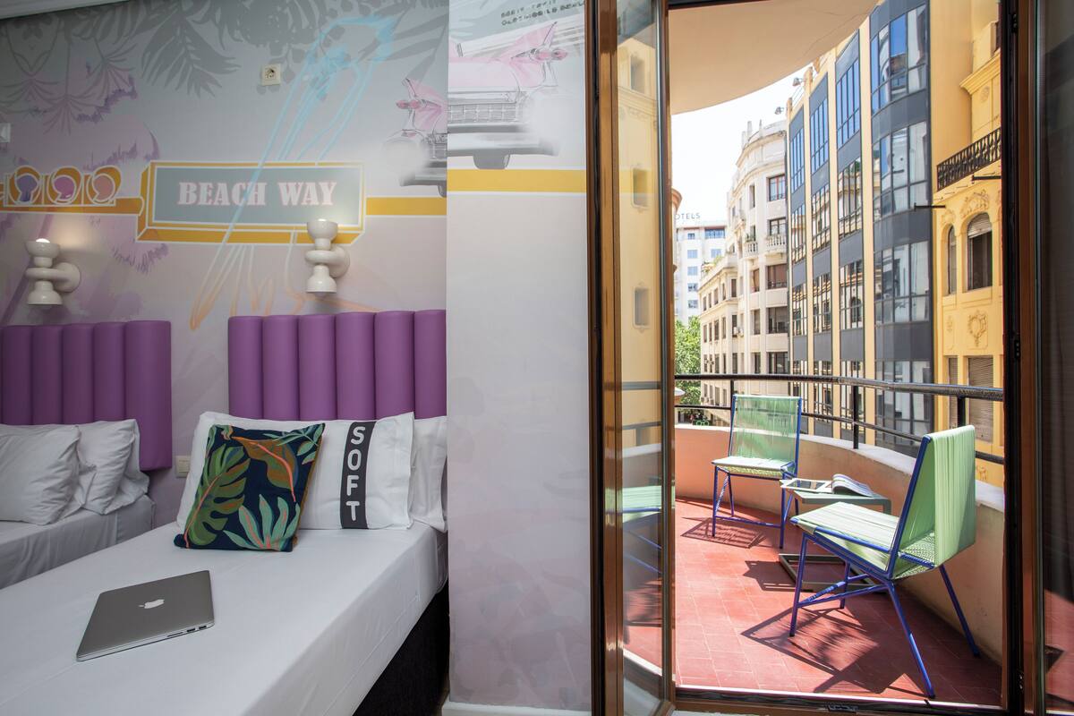 Une chambre d’hôtel avec un lit, un ordinateur portable et une vue sur la ville, visible à travers une porte vitrée.