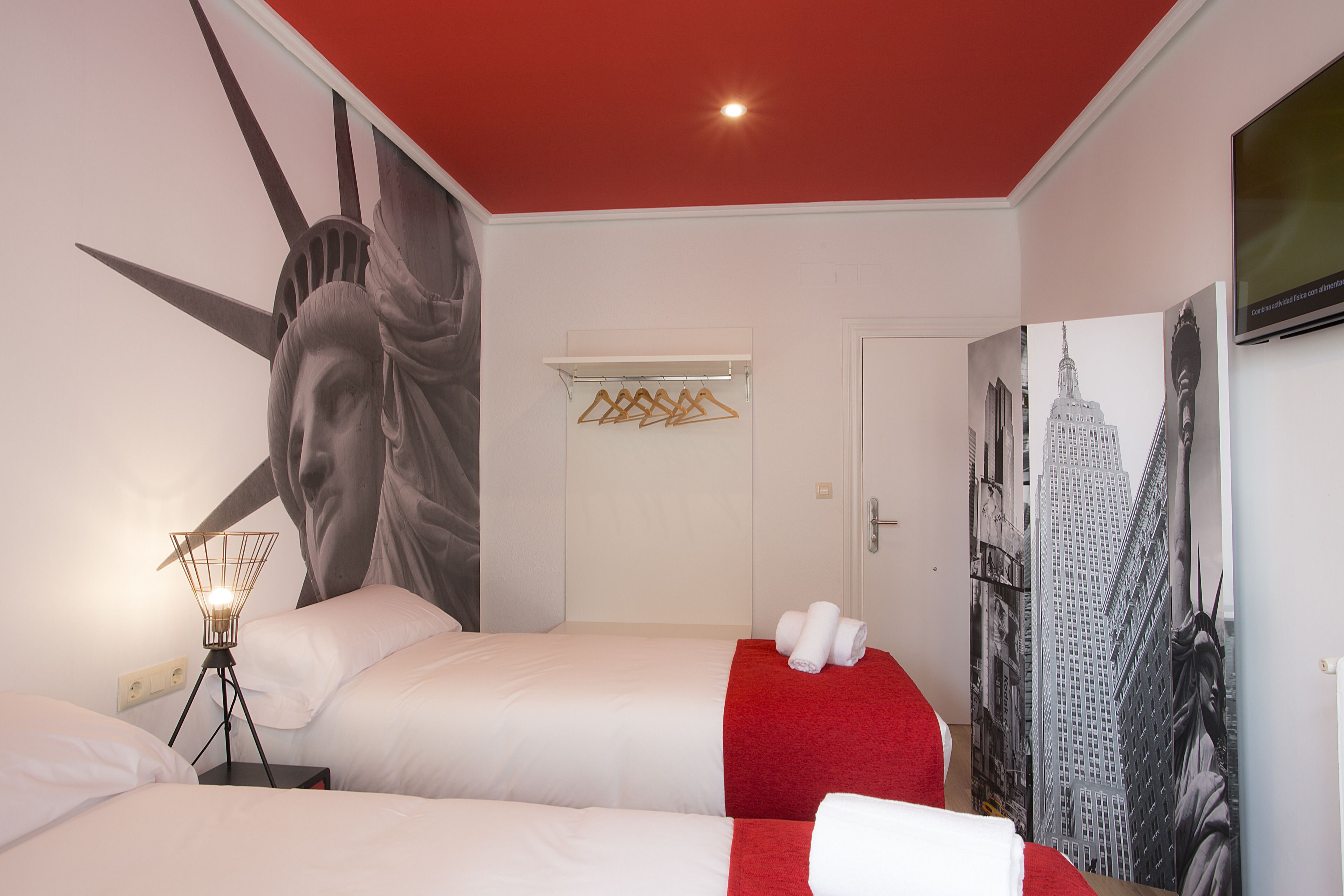 Una habitación de hotel con cama, mesita de noche, televisor montado en la pared y una puerta.