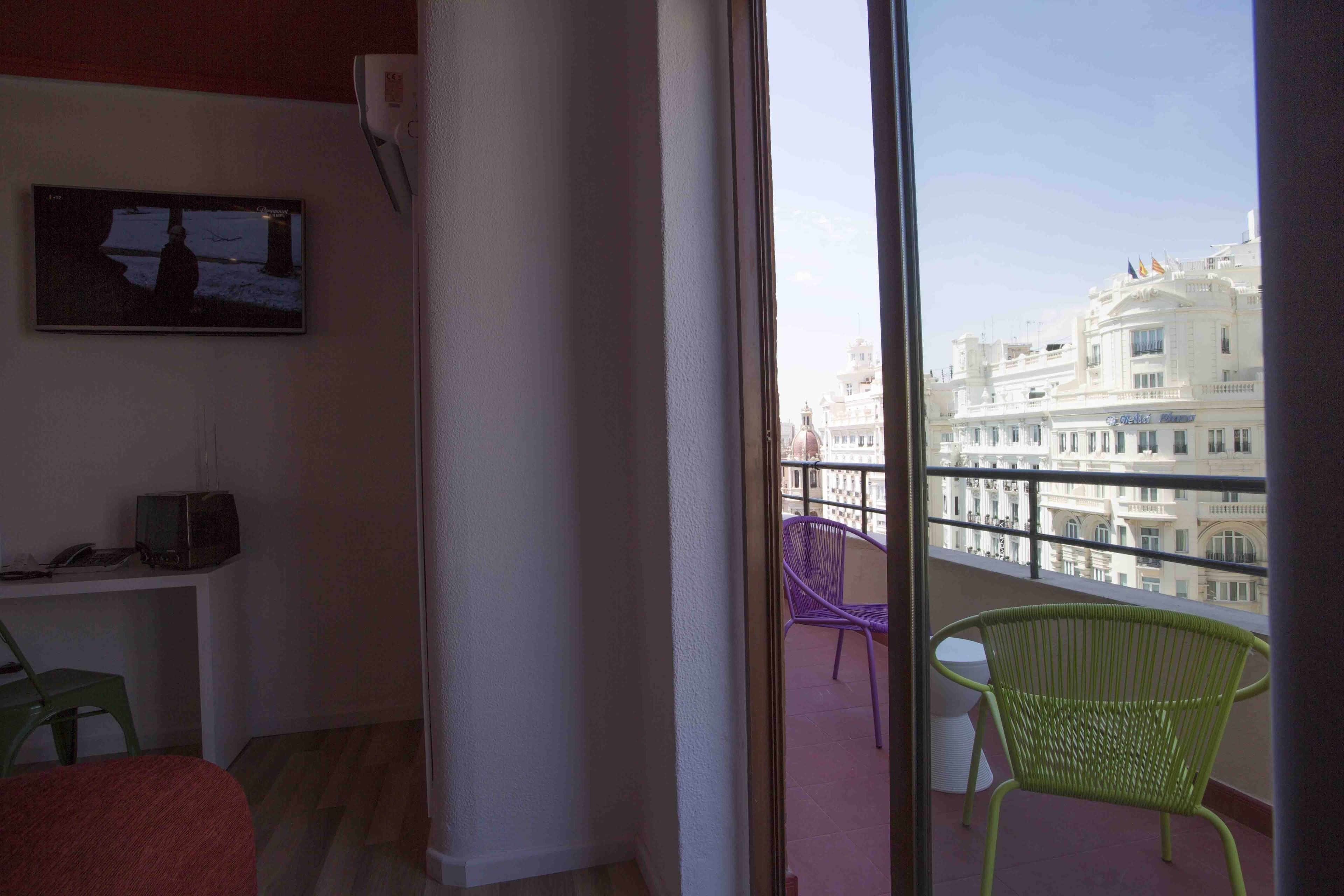 Un balcón con vistas a un edificio blanco, un televisor en la pared y una silla.