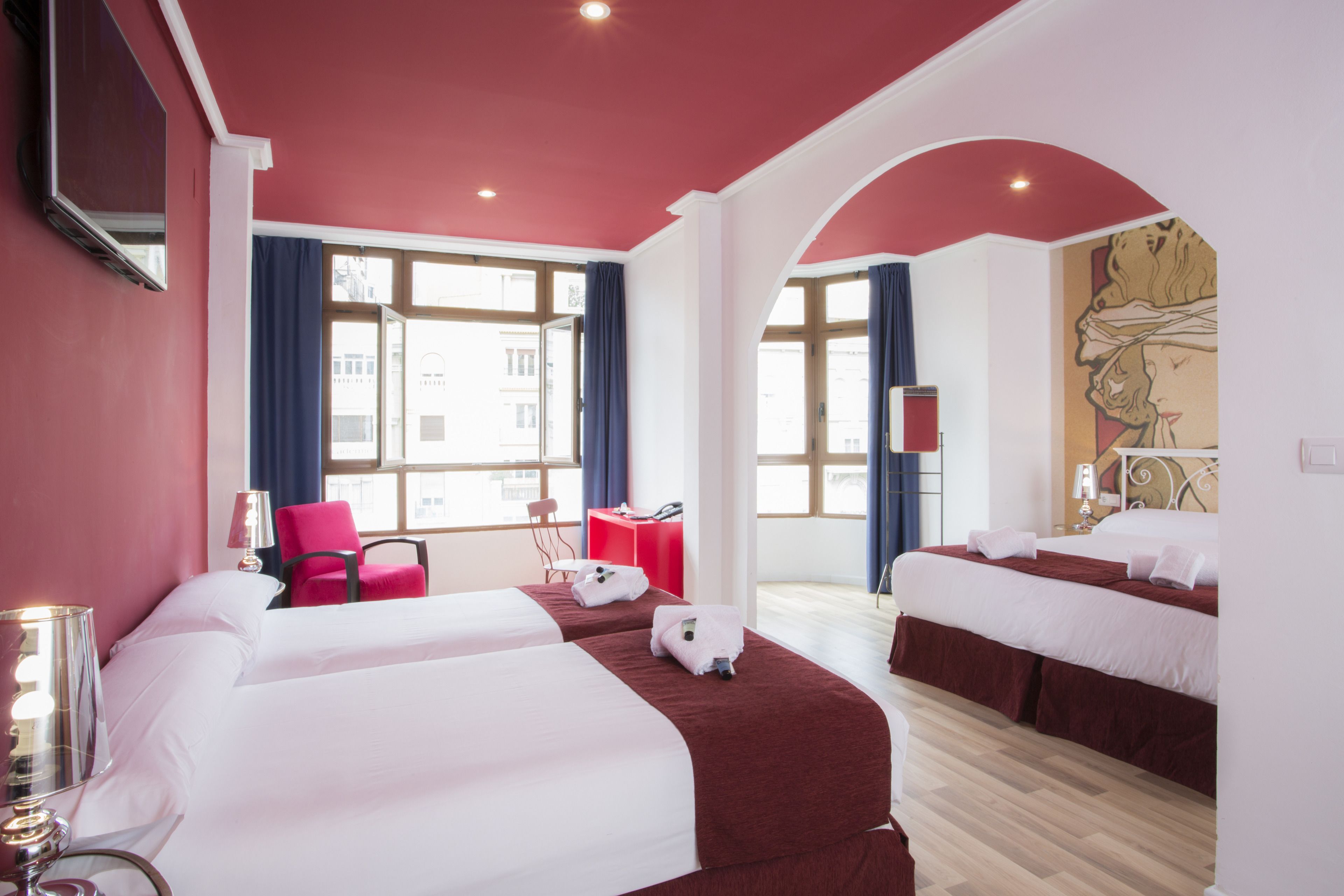 A hotel room with two beds, a desk, a chair, and a large window.