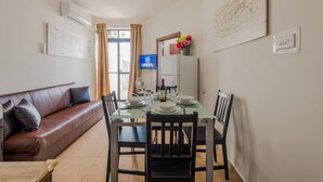 Een moderne woonkamer met een bruine leren bank, een eettafel gedekt voor vier personen, en een flatscreen televisie aan de muur.