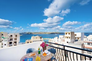 A balcony with a table set for breakfast overlooking a coastal cityscape. - Seashells 2 bedroom Apartment with sunny terrace with stunning panoramic sea views by Getaways Malta (St. Paul's Bay)