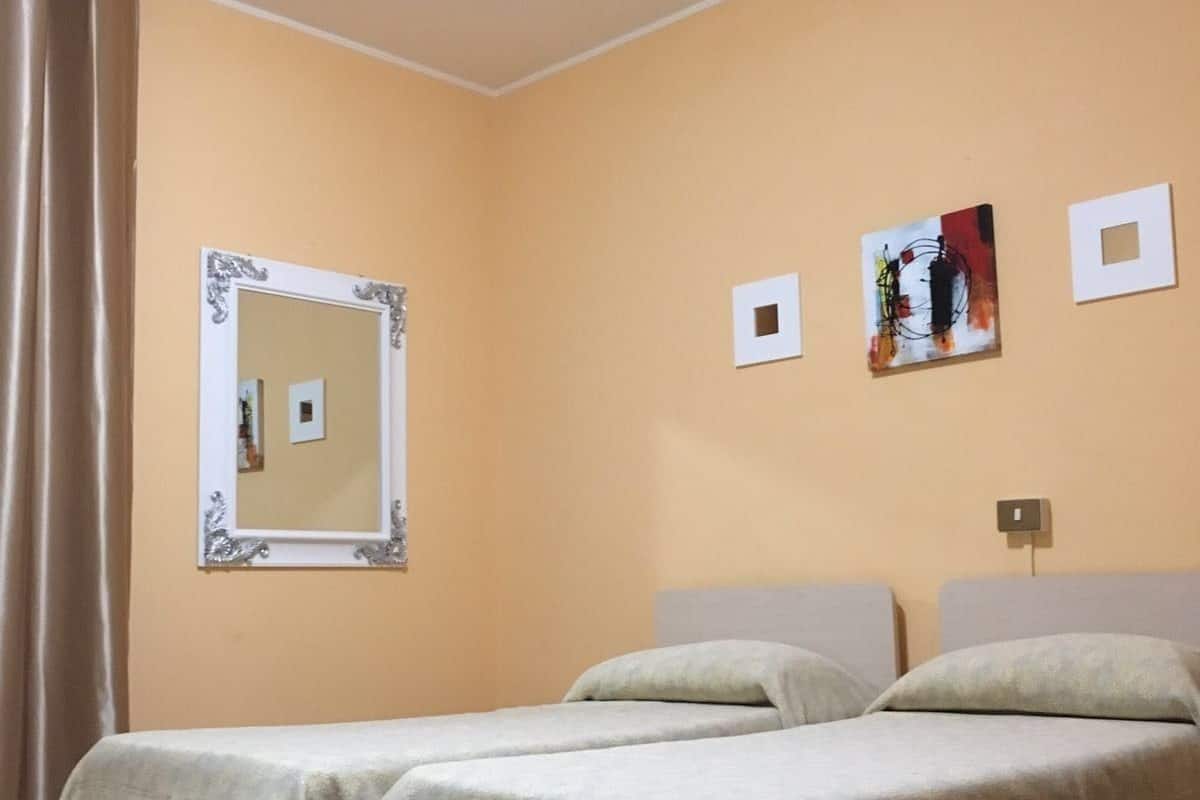 A hotel room with two beds, a mirror, and three framed pictures on the wall.