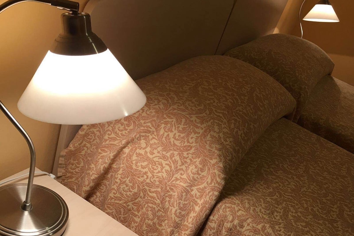 A neatly made bed with patterned bedding, a bedside lamp, and a wooden nightstand.