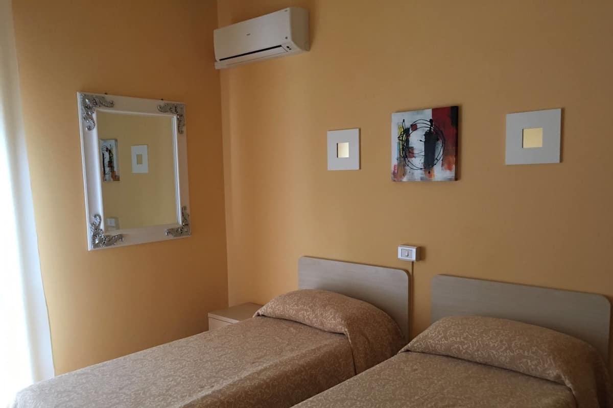 A hotel room with two beds, an air conditioning unit, a mirror, and artwork on the wall.