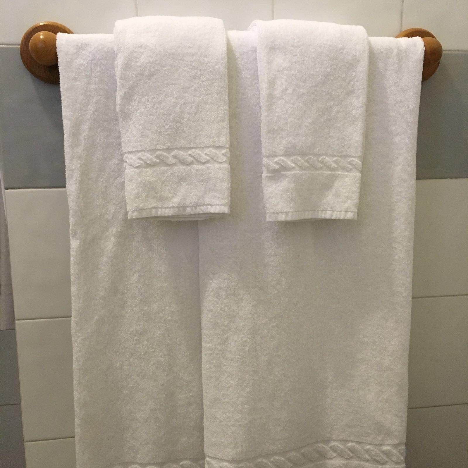 Due asciugamani bianchi appesi a un portaserviti di legno in un bagno con pareti piastrellate.