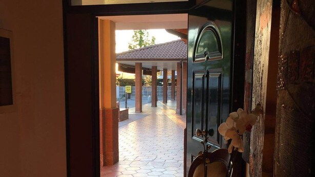 A hotel entrance with a tiled floor leading to an outdoor area, a round table with a vase of flowers, and a door with a decorative handle. - Hotel Commercio (Campogalliano)