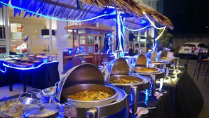 Een buffetopstelling met meerdere aanzitpunten, afgedekt met metalen deksels, en verlicht met blauw sfeervol licht.