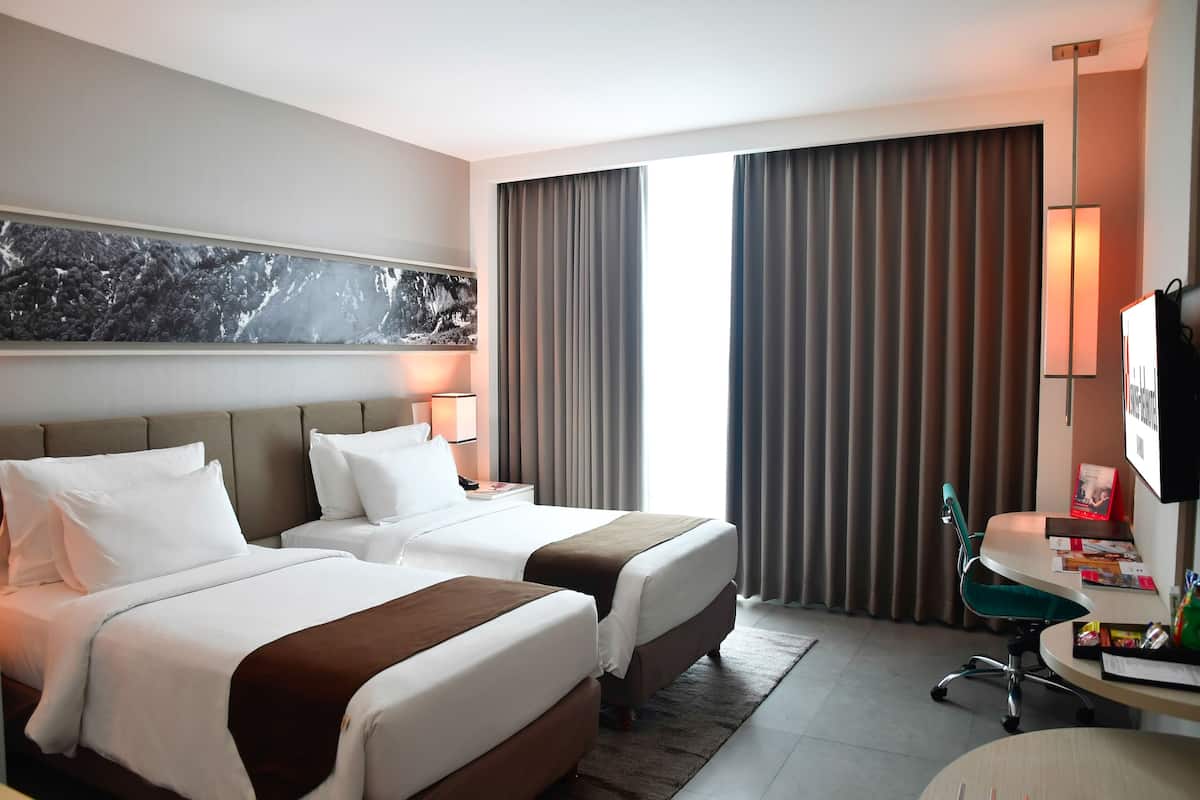 Une chambre d’hôtel avec deux lits, un bureau, une chaise, une télévision et une grande fenêtre avec des rideaux.