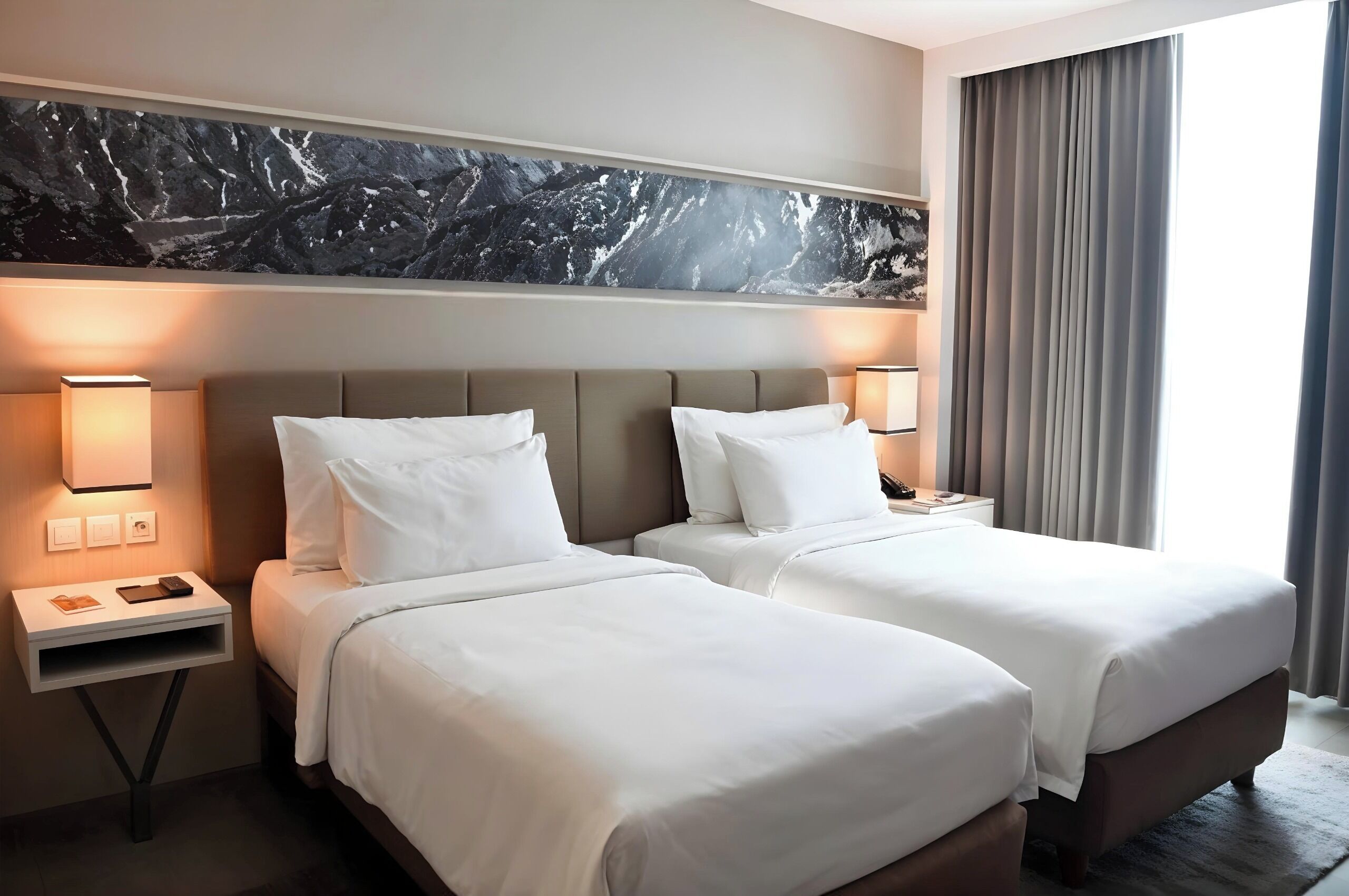 A hotel room with two beds, a marble headboard, bedside lamps, and a large window with curtains.