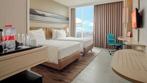 Hotelkamer met twee bedden, een bureau, een stoel, een televisie en een groot raam met uitzicht op de stad.