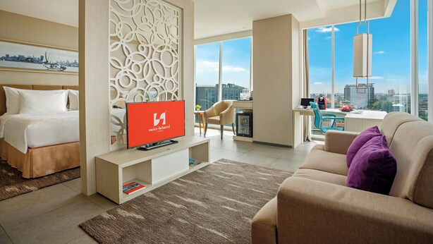Een moderne hotelkamer met een bed, een televisie, een bureau en een groot raam met uitzicht op de stad.