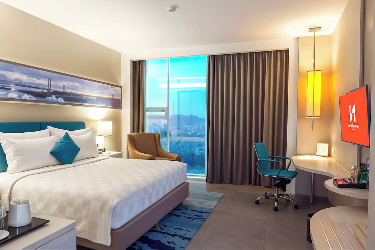 Une chambre d’hôtel avec un grand lit, un bureau, une chaise, une télévision et une vue sur la ville par la fenêtre.