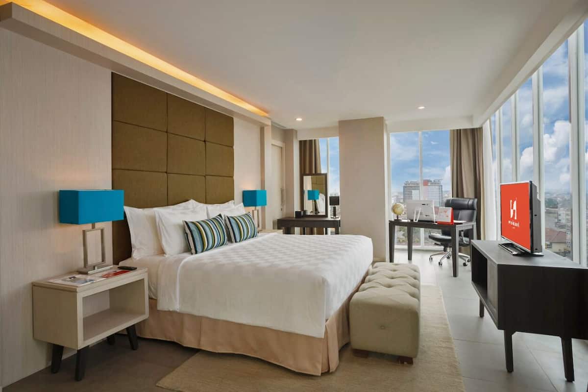 Une chambre d’hôtel moderne dotée d’un grand lit, d’un bureau, d’une télévision et offrant une vue sur la ville.