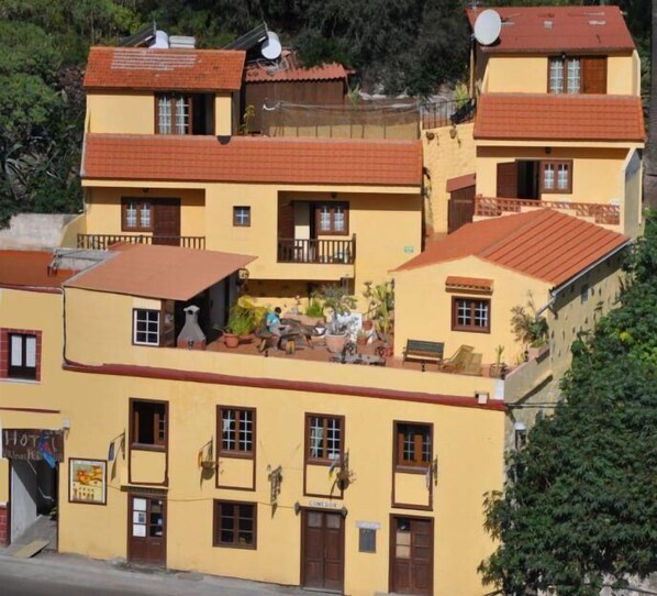 A multi-story hotel with balconies, a rooftop terrace, and a sign indicating a restaurant.