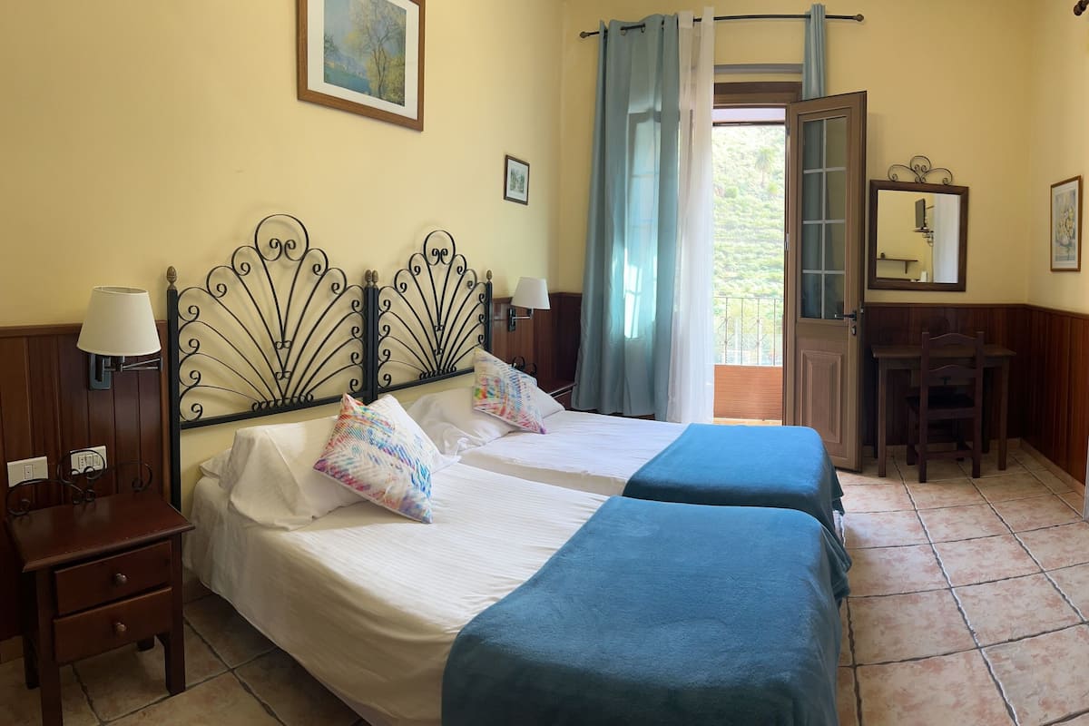 A bedroom with two beds, a desk, a chair, a television, and a window with curtains.