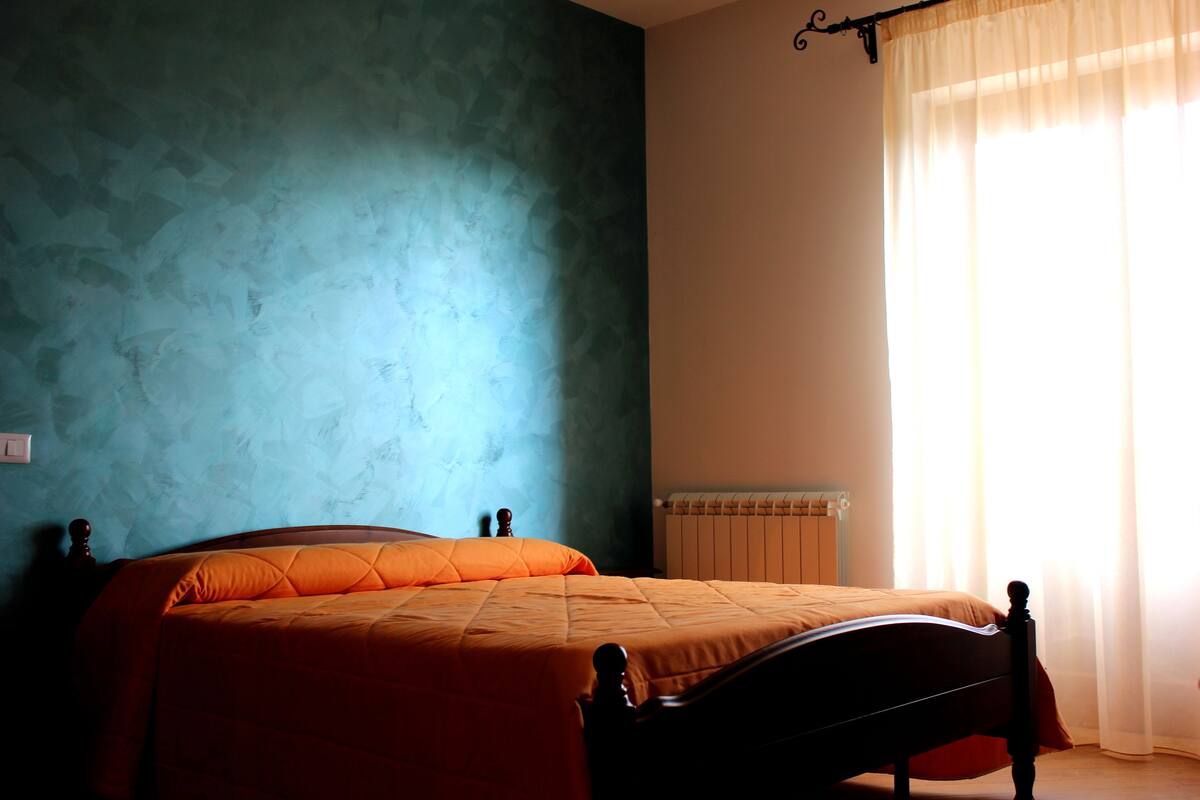 A bedroom with a bed, a nightstand, and a window with curtains.
