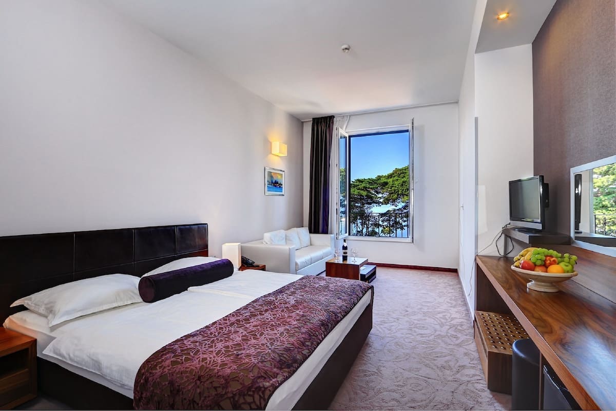 A hotel room with a large bed, a sofa, a TV, and a fruit bowl.