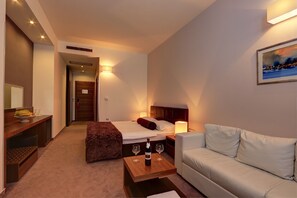 A hotel room with a bed, a sofa, a wooden table with two wine glasses and a bottle, and a painting on the wall. - Hotel Lipa (Postira)