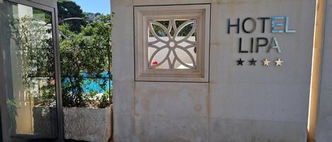L’entrée d’un hôtel, avec une enseigne indiquant « HÔTEL LIPA » et une fenêtre décorative.