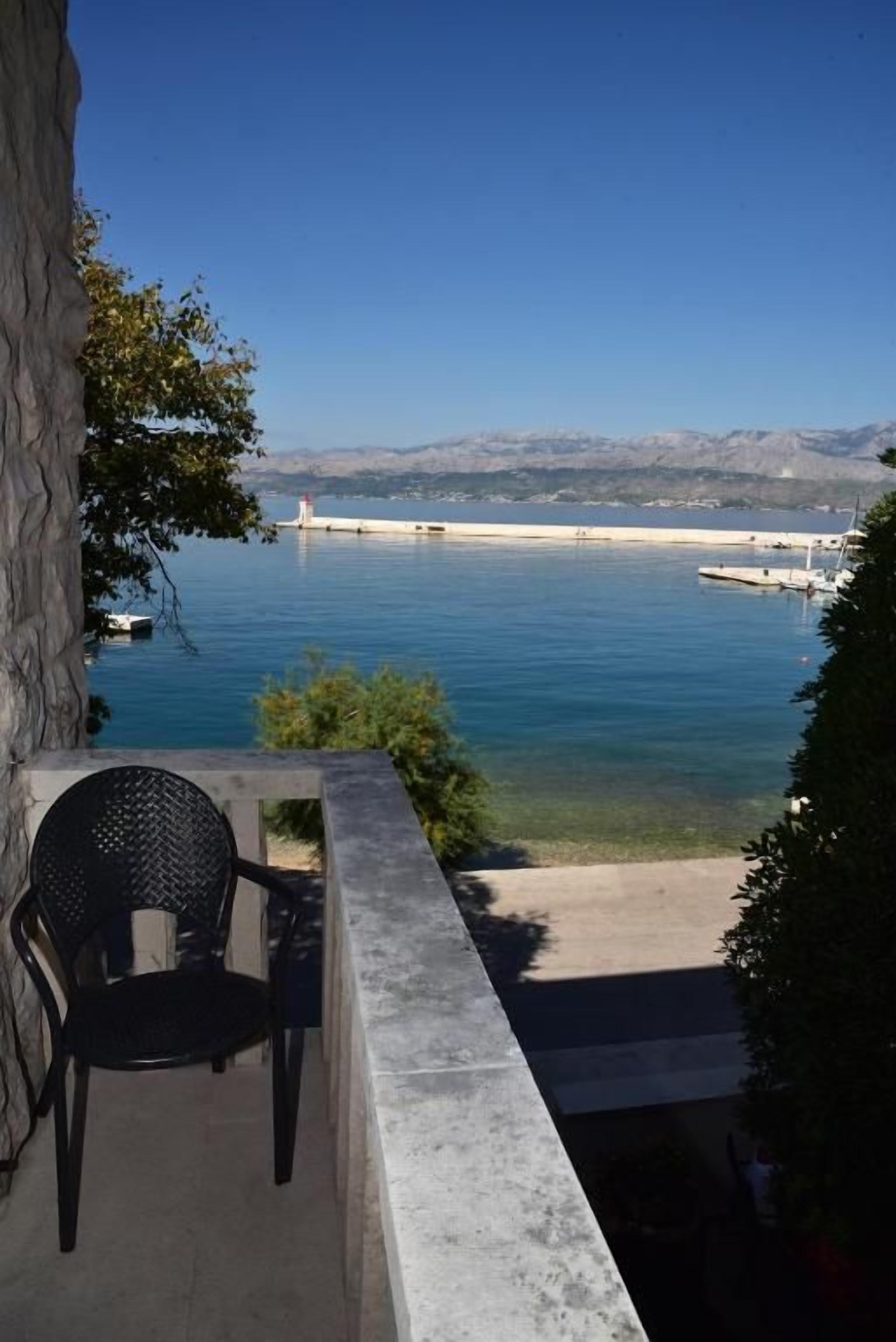 A balcony with a view of a calm body of water, a distant shoreline, and a clear sky.