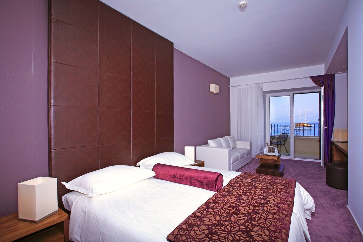 A hotel room with a large bed, a sofa, a small table, and a view of the outside.