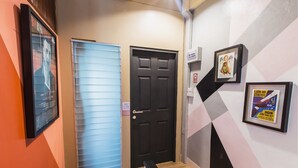 A hallway with a black door, a framed poster on the wall, and a blue window. - Bharani Hostel (Bangkok)