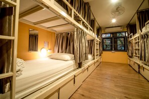 A dormitory room with bunk beds, a ceiling fan, a window with curtains, and a bedside lamp. - Bharani Hostel (Bangkok)